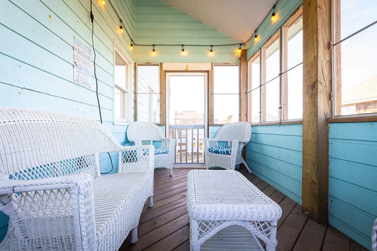 A covered porch with wicker furniture and string lights.