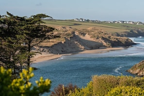 A coastal landscape with a sandy beach, a clear blue sea, and rolling hills in the background.
