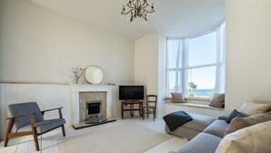 Una sala de estar con chimenea, televisor y zona de estar con vista al océano.