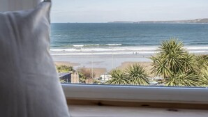 Vista desde una ventana sobre una playa con palmeras y cielo despejado.