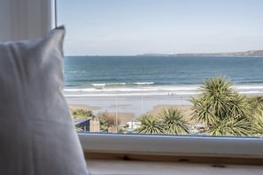 A view from a window overlooking a beach with palm trees and a clear sky. - Spacious House, Sea Views Opposite Beach (Newquay)