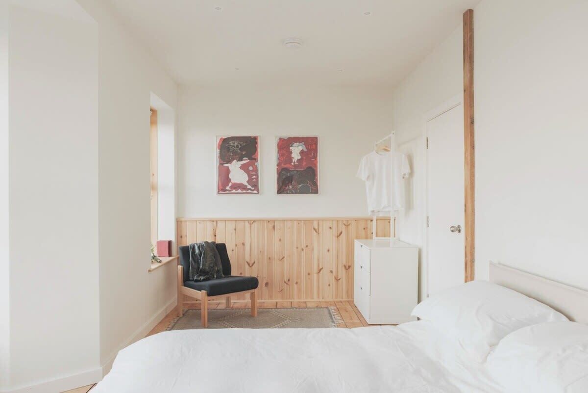 Une chambre à coucher comprenant un lit, une chaise, une armoire et deux œuvres d’art accrochées au mur.