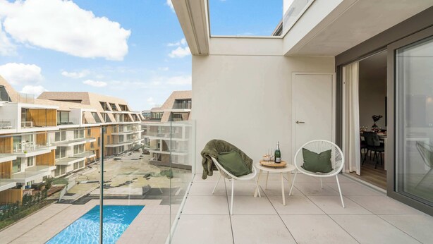 Un appartement moderne doté d’un balcon en verre donnant sur une piscine et d’autres immeubles.