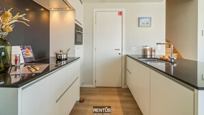 Une cuisine moderne avec des armoires blanches, un comptoir noir et un four encastré. Un vase rempli de fleurs se trouve sur le côté gauche, ainsi qu’une petite table sur laquelle sont posés une plante et un cadre photo.