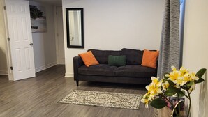 Un salon avec un canapé marron foncé, deux coussins orange, un coussin vert et un tapis à motifs.