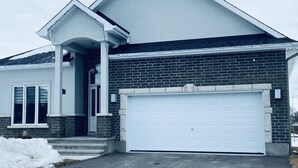 Une maison moderne à deux étages, avec une façade en briques, une porte de garage blanche et un porche abrité.