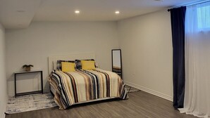 Une chambre à coucher avec un lit, une table de chevet, un miroir et une fenêtre avec des rideaux.