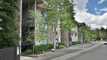 A row of modern buildings with stone facades and balconies, a clear sky, and a mountain in the background.