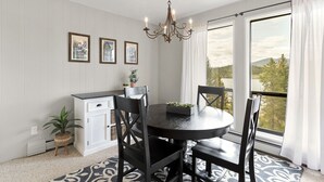 A dining area with a round table, black chairs, a chandelier, and a view of mountains through large windows.