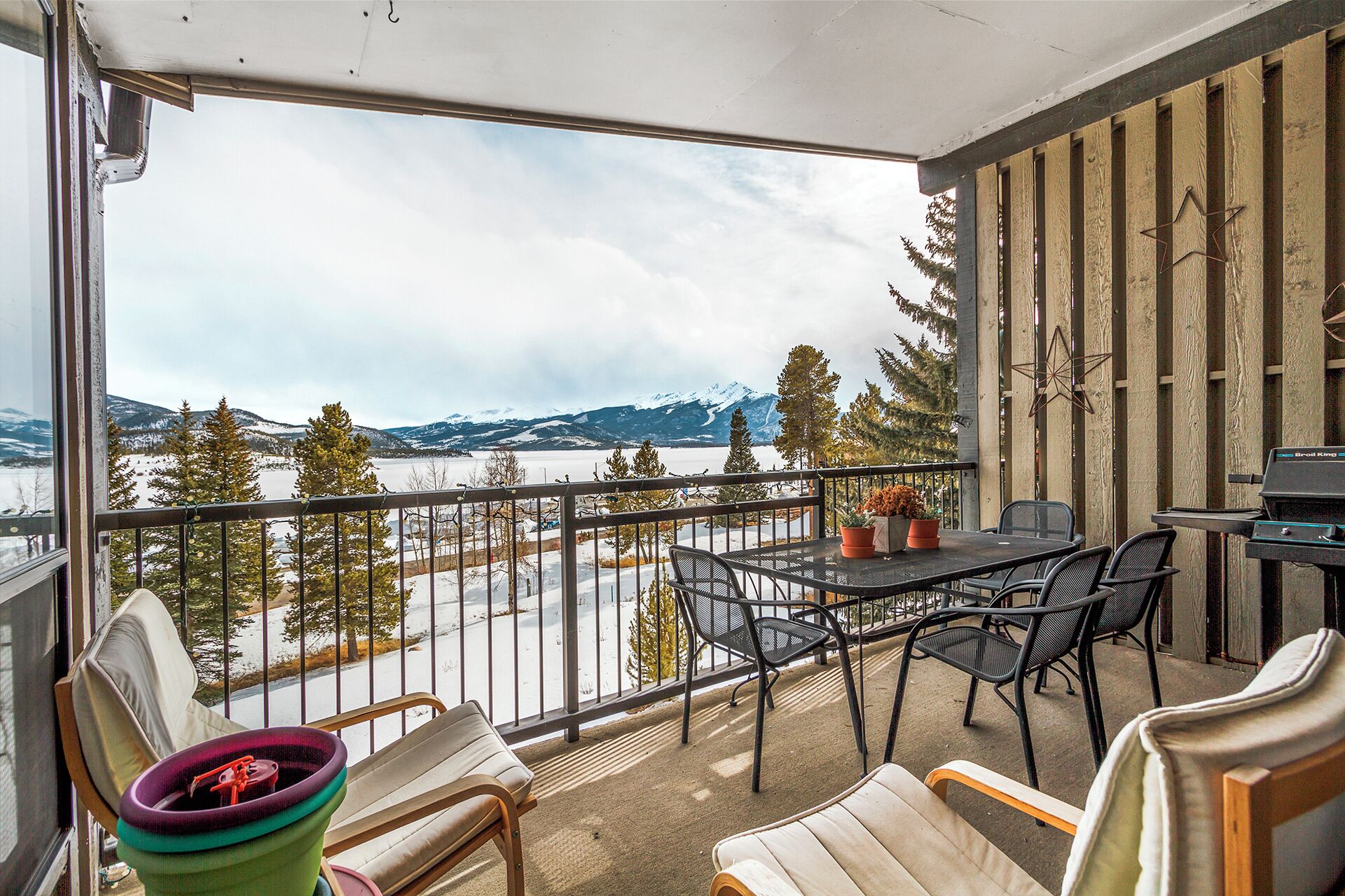 Un balcon avec une table et des chaises, donnant sur un paysage enneigé avec des montagnes et une étendue d’eau.