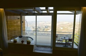 Relax on the balcony with a view of the surrounding landscape, featuring a table and chairs for dining or unwinding, and a bathtub with a shower curtain.