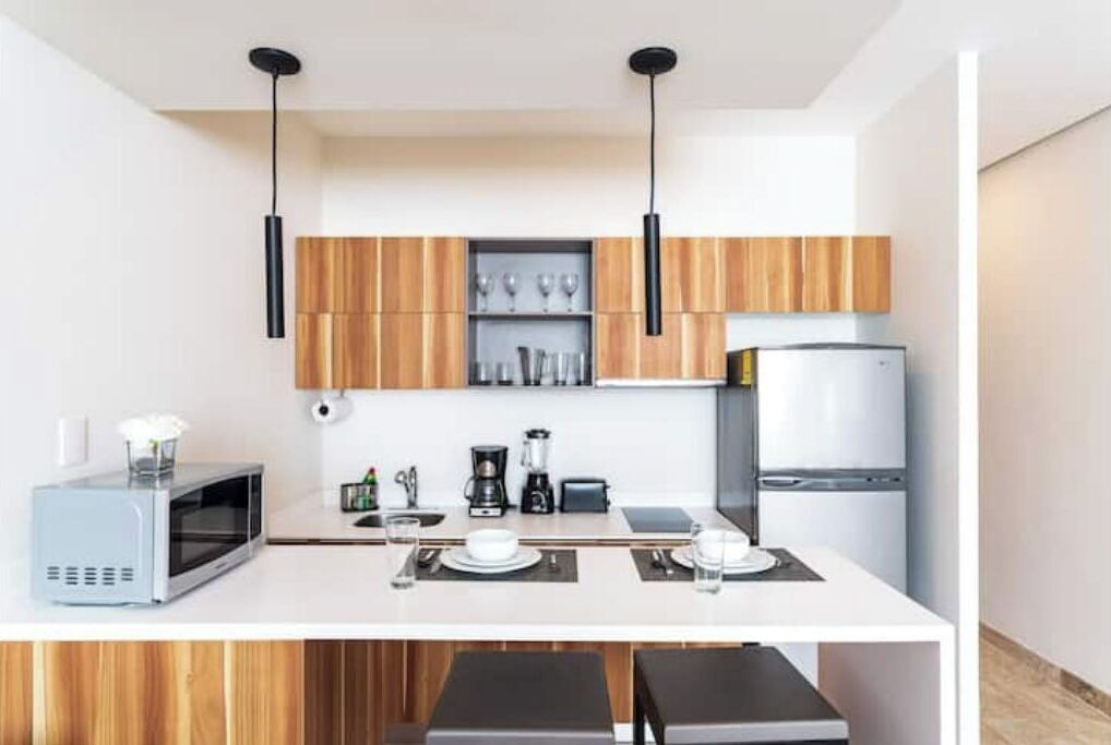 Eine moderne Küche mit Holzschränken, einer weißen Arbeitsplatte, einer Mikrowelle, einer Kaffeemaschine und einem Kühlschrank.