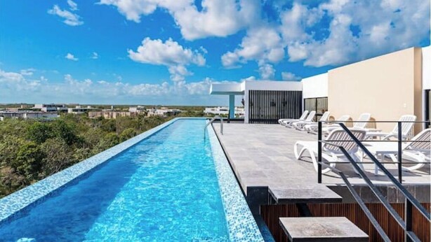 Una piscina infinita en la azotea con agua cristalina y azul, rodeada de sillones de descanso y vistas panorámicas de la ciudad.