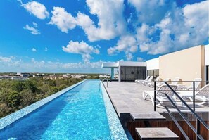 Une piscine à débordement située sur le toit, avec une eau d’un bleu cristallin, entourée de chaises longues et offrant une vue imprenable sur le paysage urbain.