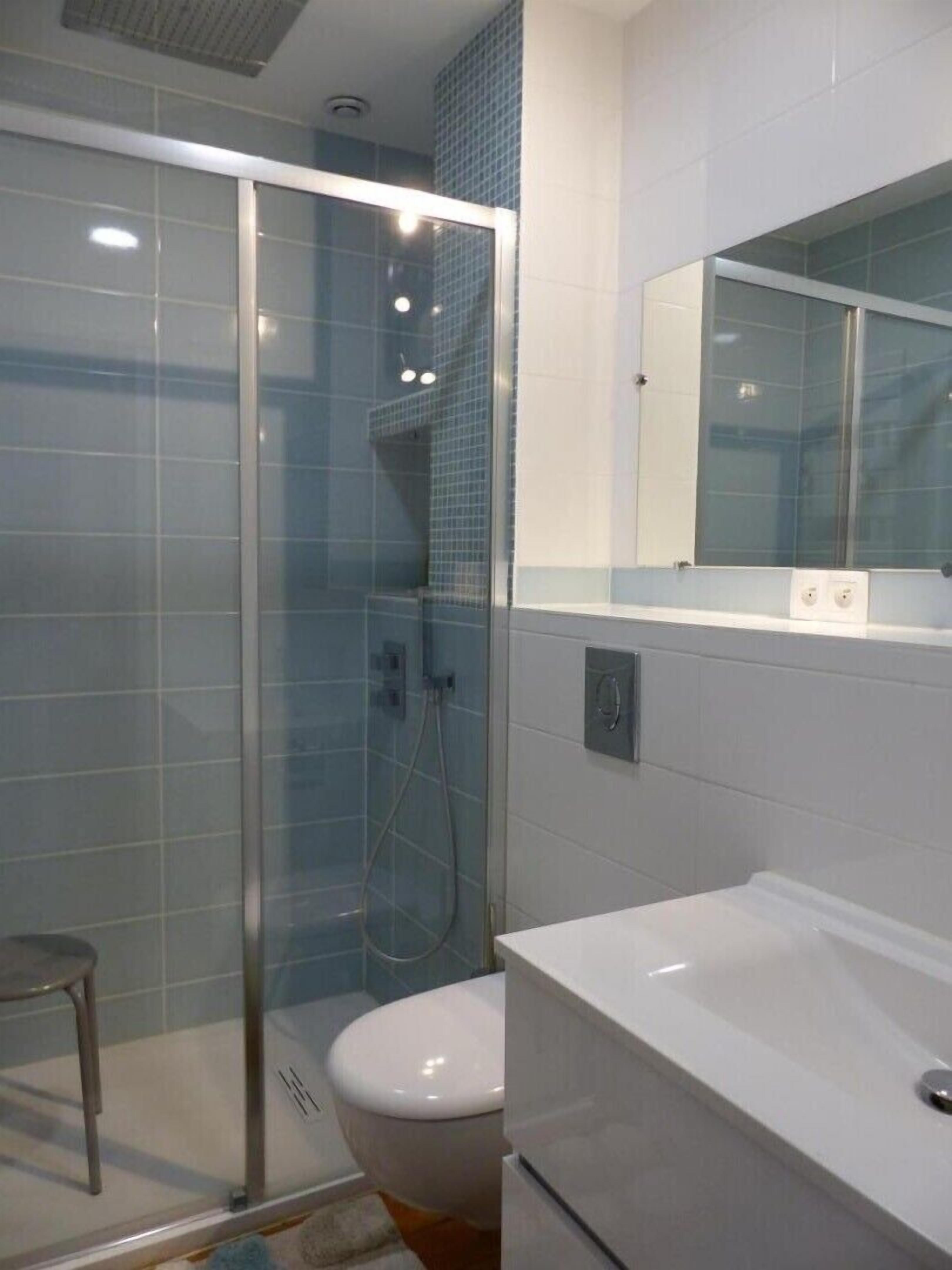 Une salle de bain moderne avec une douche à parois de verre, des toilettes blanches et un grand miroir au-dessus du lavabo.