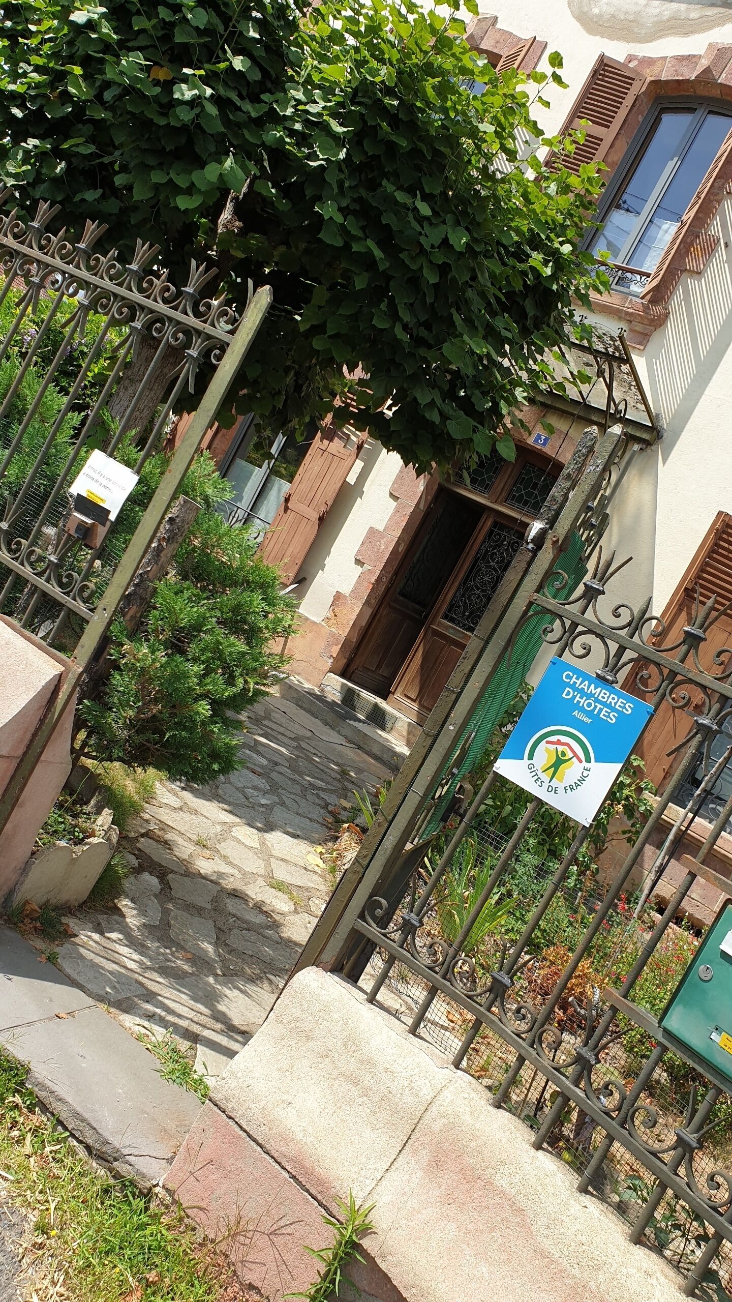 A narrow stone pathway leading to a building with a wooden door and a metal gate. A sign indicates the property is a guesthouse.