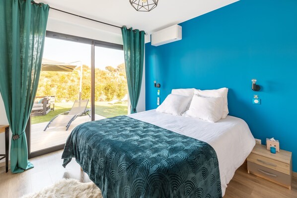 A bedroom with a large bed, a view of the outdoors, and a blue accent wall.