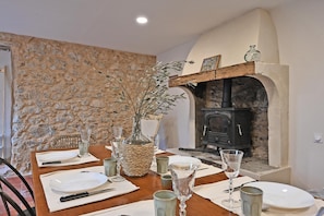 A dining table set with plates, glasses, and a vase in a room with a stone wall and a fireplace.