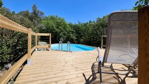 Eine Holzterrasse mit Schwimmbad, umgeben von Bäumen.