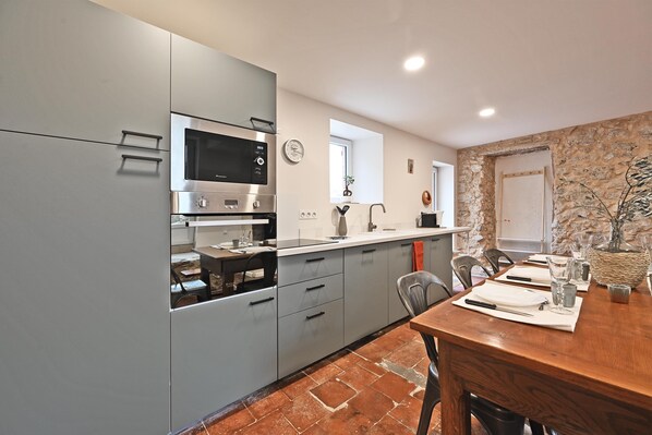 A modern kitchen with grey cabinets, a built-in oven, and a dining area with a wooden table set for two.