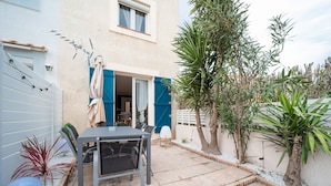 Une terrasse avec une table et des chaises, une porte bleue et un petit jardin agrémenté de plantes.