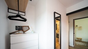Un couloir avec une commode blanche, un miroir et un cintre noir suspendu.