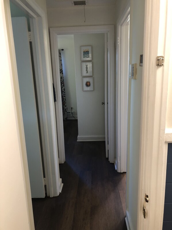 A hallway with a dark wooden floor, white walls, and a door at the end leading to another room.
