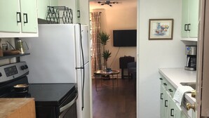 Una cocina con estufa, horno y refrigerador. Hay una mesa de comedor con sillas y un televisor montado en la pared.