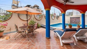 An outdoor patio with a pool, lounge chairs, a table with chairs, and potted plants.