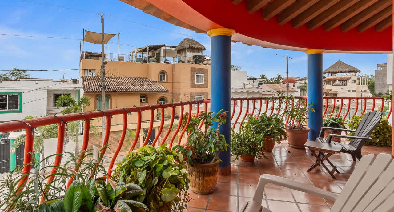 A balcony with red railings, potted plants, and a white chair.