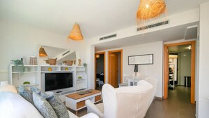 Un salon moderne avec des meubles blancs, un téléviseur et une cheminée. Deux lampes suspendues et un tableau encadré ornent le mur.