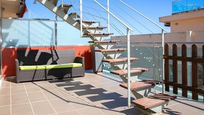 Une terrasse sur le toit avec un canapé en osier, un escalier et une rambarde en verre.