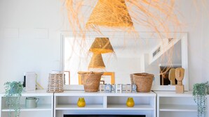 Un salon moderne avec une cheminée blanche, des paniers en osier et un grand miroir qui reflète la pièce.