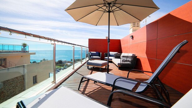 Un balcon équipé d’un grand parasol, de deux fauteuils de jardin et d’une table.