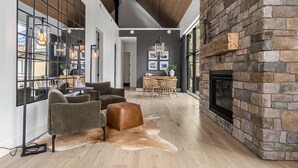 A modern living room with a stone fireplace, leather sofa, and a dining area with a wooden table and chairs. - Spectacular 8-BDRM, 8-BATH Mountain Retreat! (Canmore)