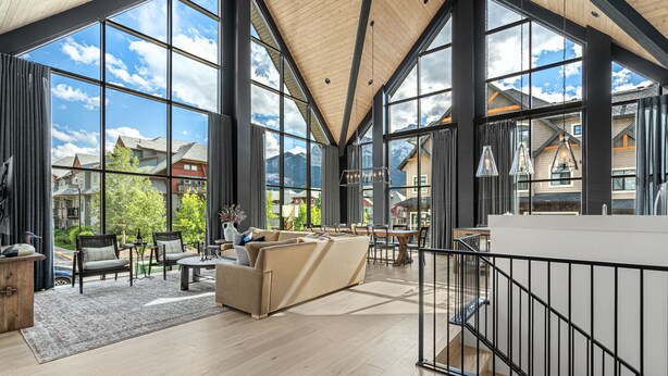 A spacious interior with large windows, a wooden ceiling, and a view of surrounding buildings and mountains. - Spectacular 8-BDRM, 8-BATH Mountain Retreat! (Canmore)