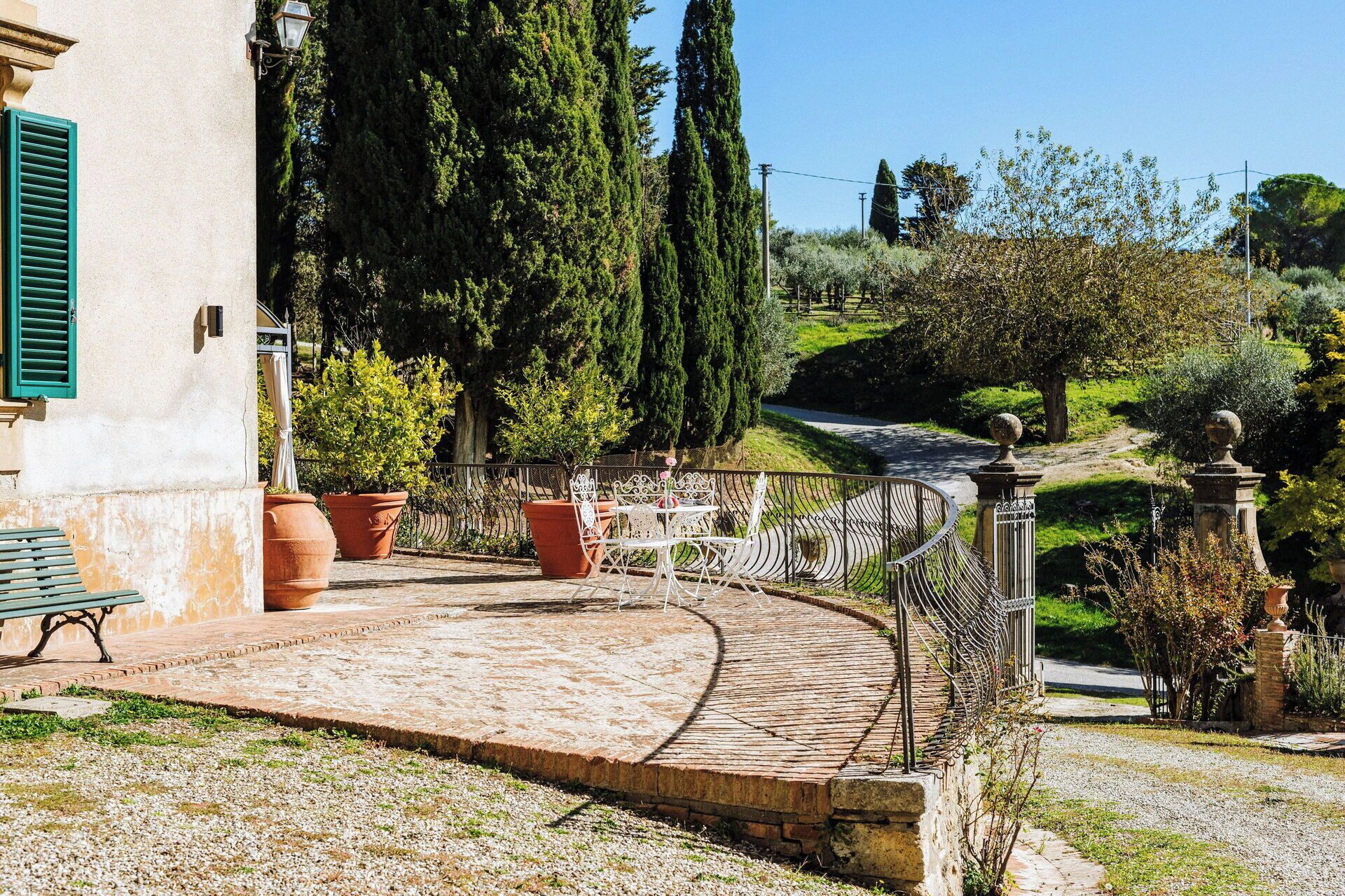 Un espace extérieur aménagé avec un revêtement pavé, un chemin sinueux, des plantes en pot et un banc.