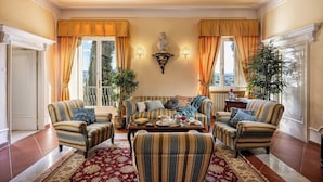 A spacious living room with a sofa set, a coffee table, and two side tables. There are two large windows with curtains, a wall-mounted lamp, and a statue. - Wonderful private villa with WIFI, A/C, private pool, patio and panoramic view, close to Siena (Poggibonsi)