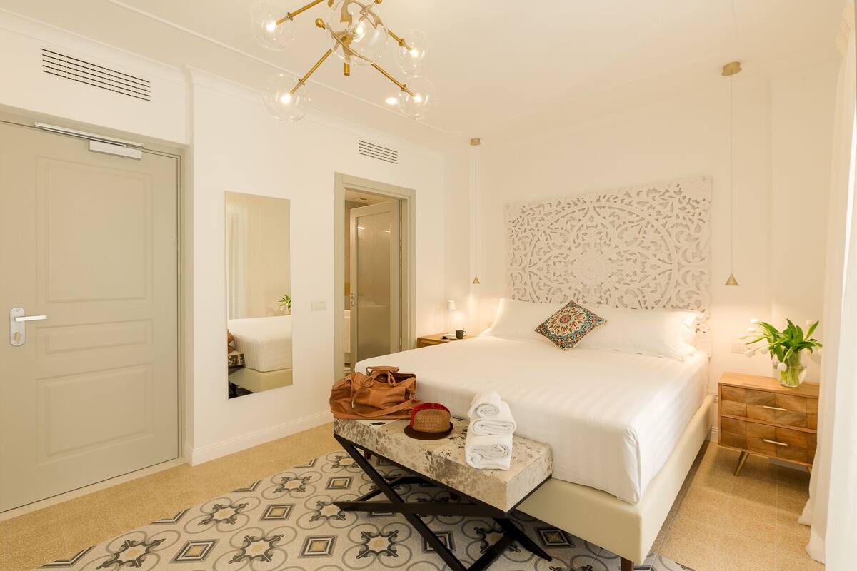 A hotel room with a bed, bedside table, and a mirror.