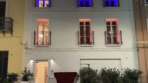 A multi-story building with balconies, a red awning, and potted plants at the entrance.