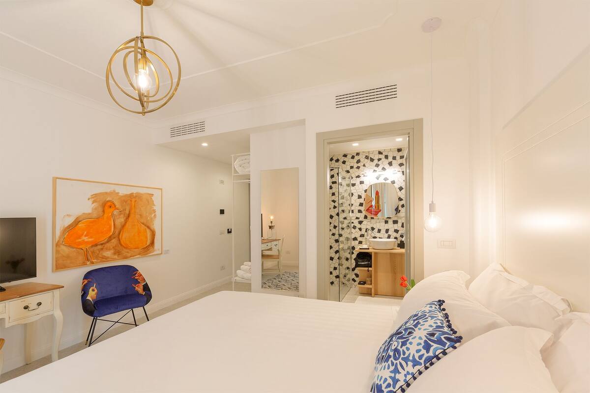 A modern hotel room with a large bed, a desk with a chair, a television, and a unique artwork on the wall.