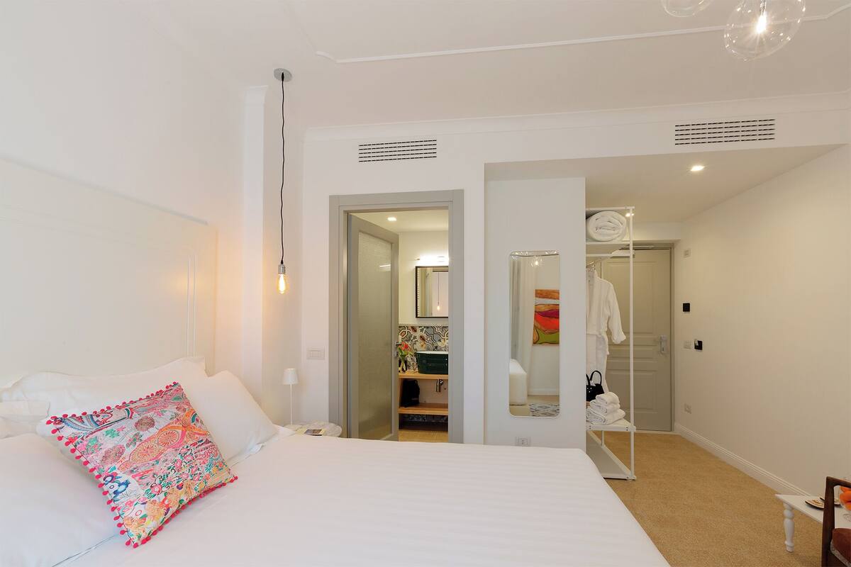 A hotel room with a bed, a colorful pillow, a wardrobe, and a mirror.