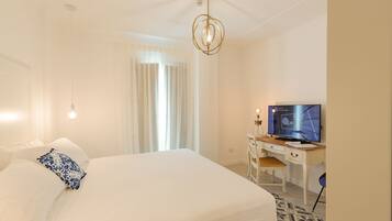 A hotel room with a bed, a desk with a television, and a chandelier.