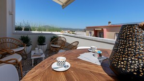 A terrace with wicker chairs, a wooden table, and a view of the cityscape.