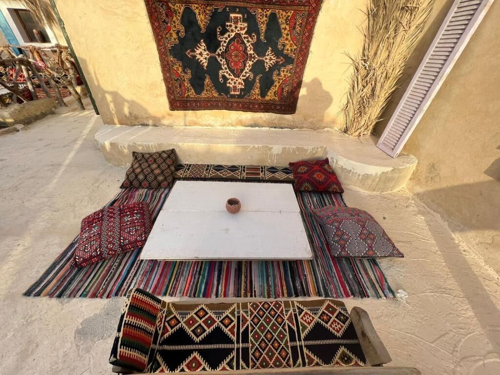 Ein gemütlicher Sitzbereich im Freien mit einem weißen Tisch, gemusterten Kissen und einem dekorativen Teppich.