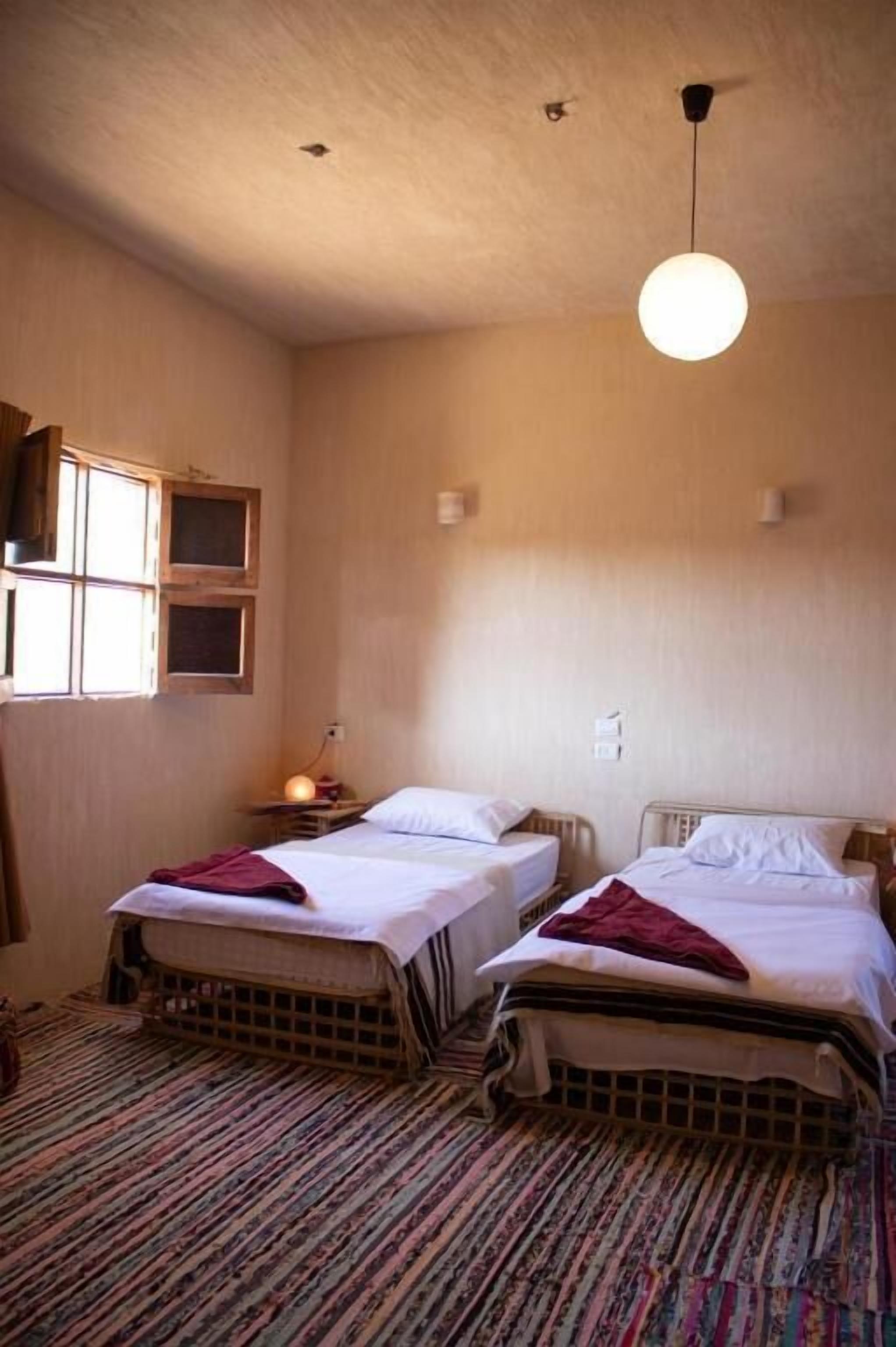 Una habitación con dos camas, un suelo estampado, un candelabro colgante y una ventana con contraventanas de madera.