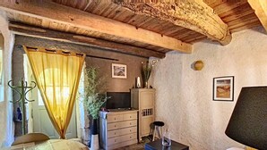 Ein gemütliches Zimmer mit Holzbalkendecke, einem Bett, einem Schreibtisch, einem Sessel, einem kleinen Tisch und einem Schrank.