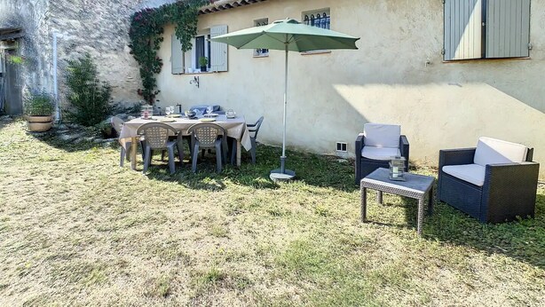 Eine Terrasse im Freien mit Esstisch, umgeben von Korbstühlen und einem grünen Sonnenschirm.