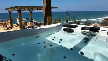 Jacuzzi con vista al océano, pérgola de madera y sillas de descanso.