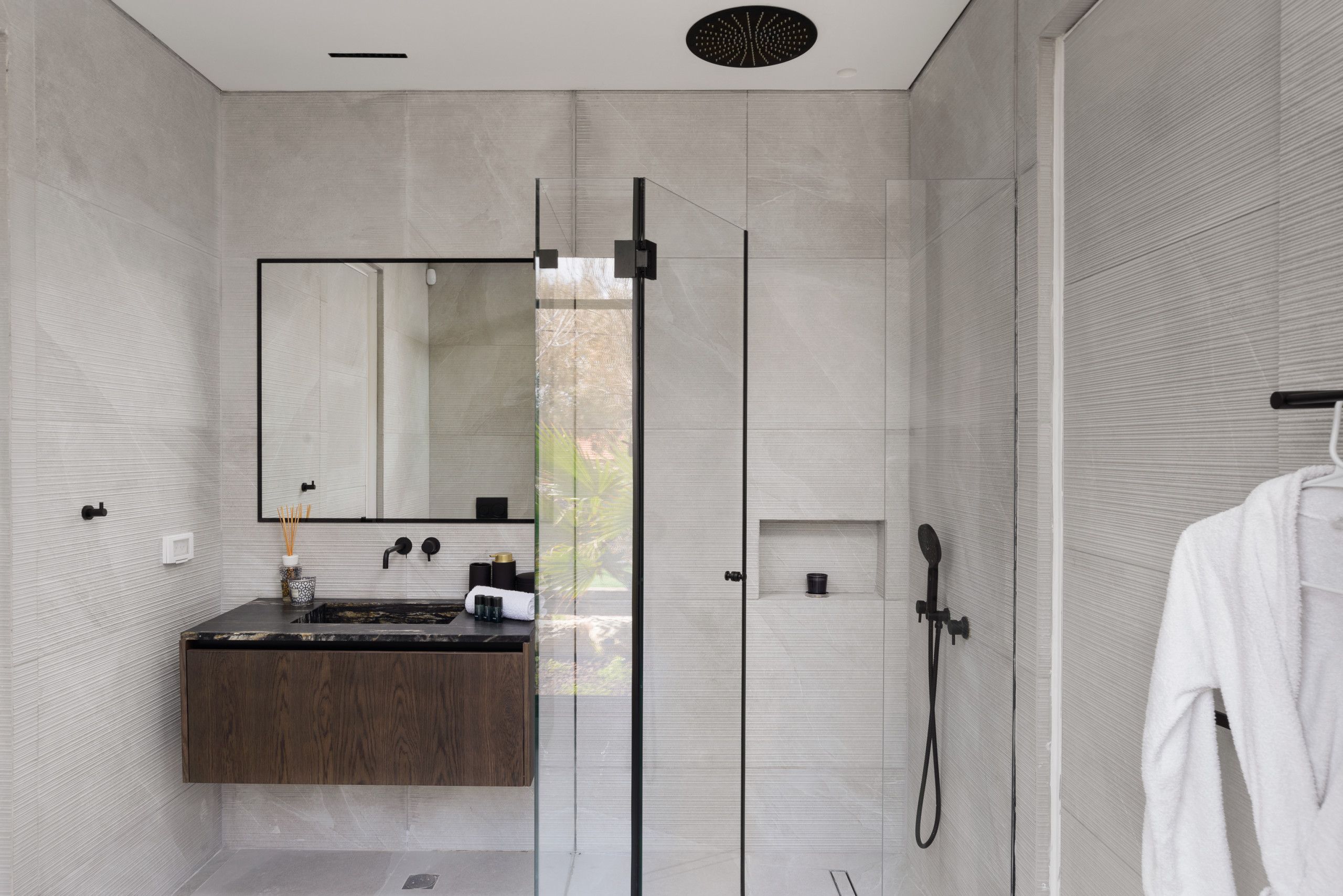 A modern bathroom with a glass-enclosed shower, a wooden vanity, and a white robe hanging on a rack.